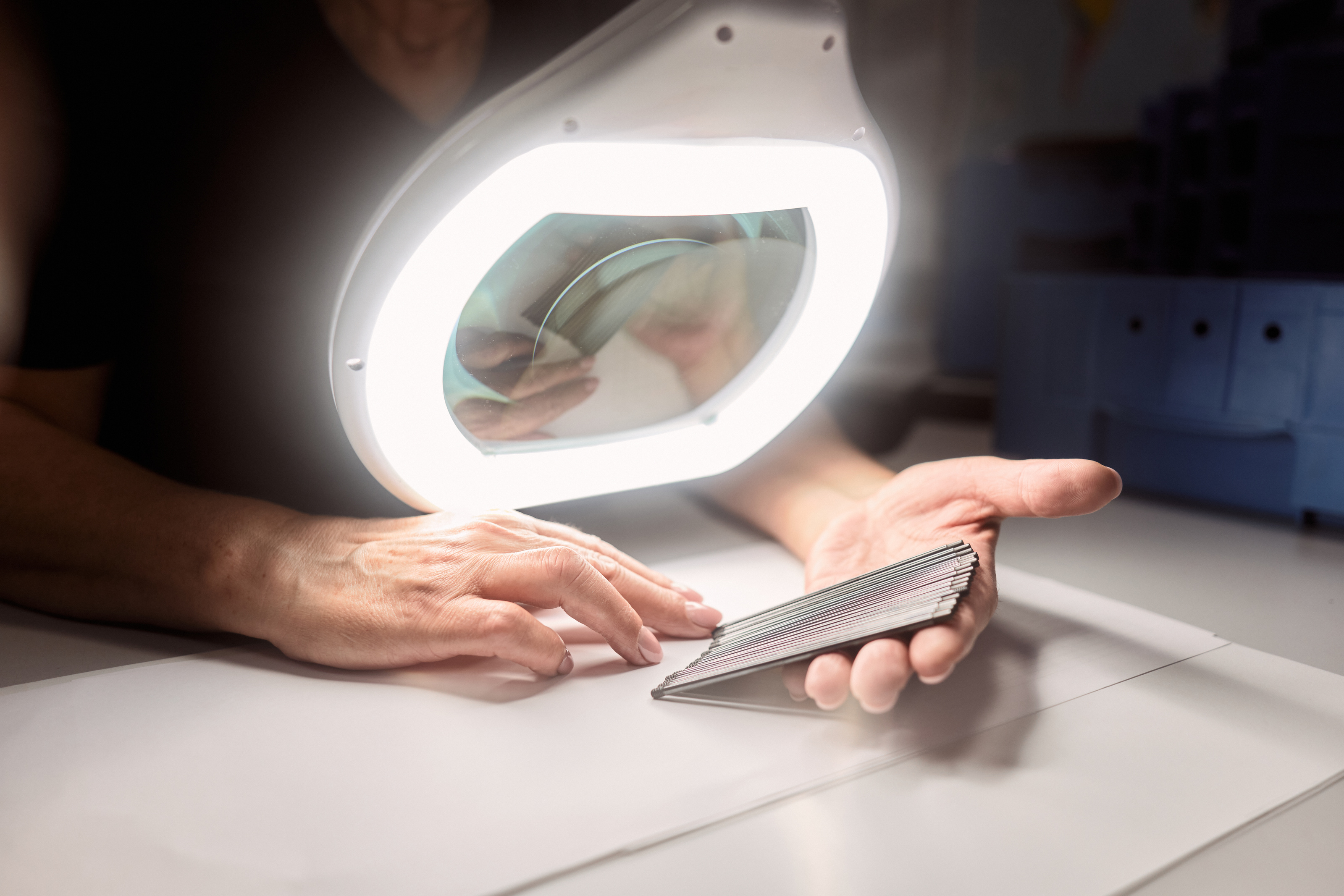 Mitarbeiter überprüft unter einer beleuchteten Lupenlampe präzise Metallkomponenten auf Qualität und Genauigkeit.