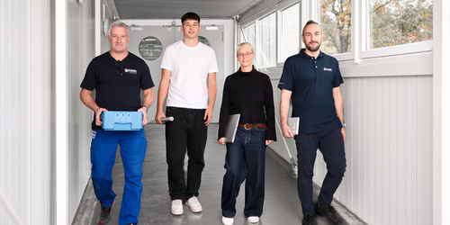 Vier Mitarbeiter:innen von Hahn Gasfedern gehen gemeinsam durch hellen Gang – Teamarbeit und Innovation.