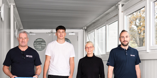 Vier Mitarbeiter:innen von Hahn Gasfedern gehen gemeinsam durch hellen Gang – Teamarbeit und Innovation.