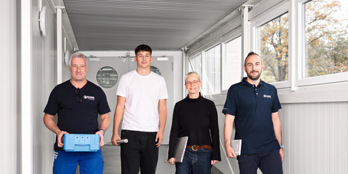 Vier Mitarbeiter:innen von Hahn Gasfedern gehen gemeinsam durch hellen Gang – Teamarbeit und Innovation.