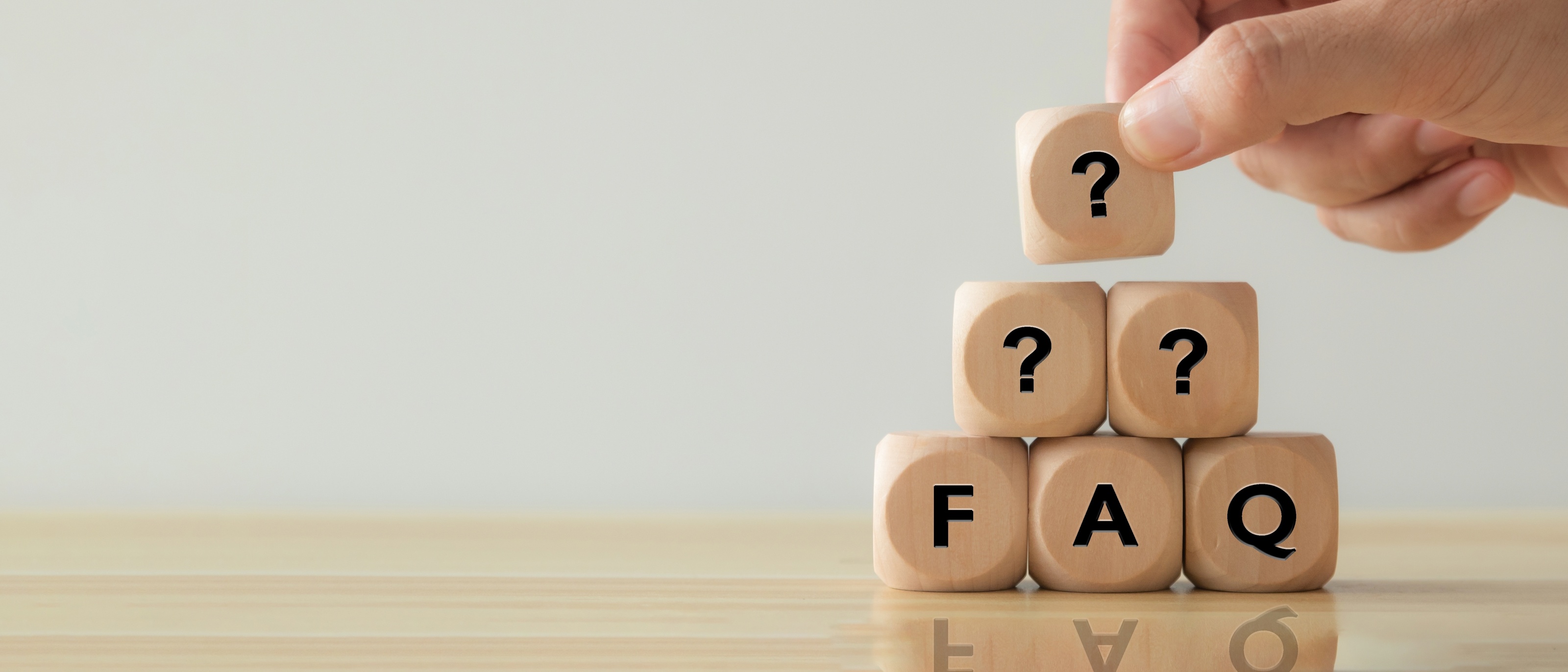 Holzwürfel mit 'FAQ' und Fragezeichen, symbolisiert häufig gestellte Fragen und Antworten für Kundeninformationen.