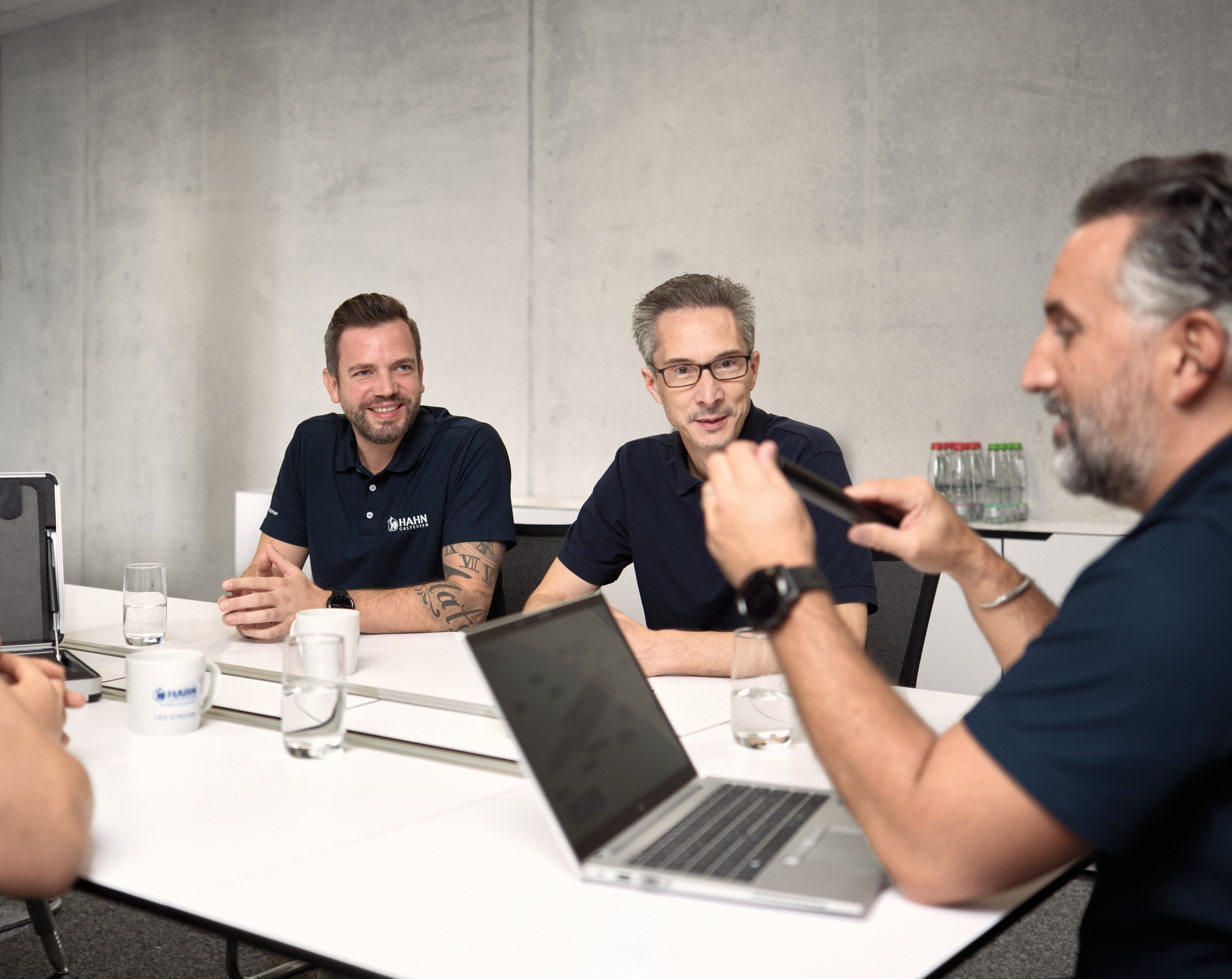 Drei Mitarbeiter:innen besprechen sich am Tisch mit Laptop und Unterlagen