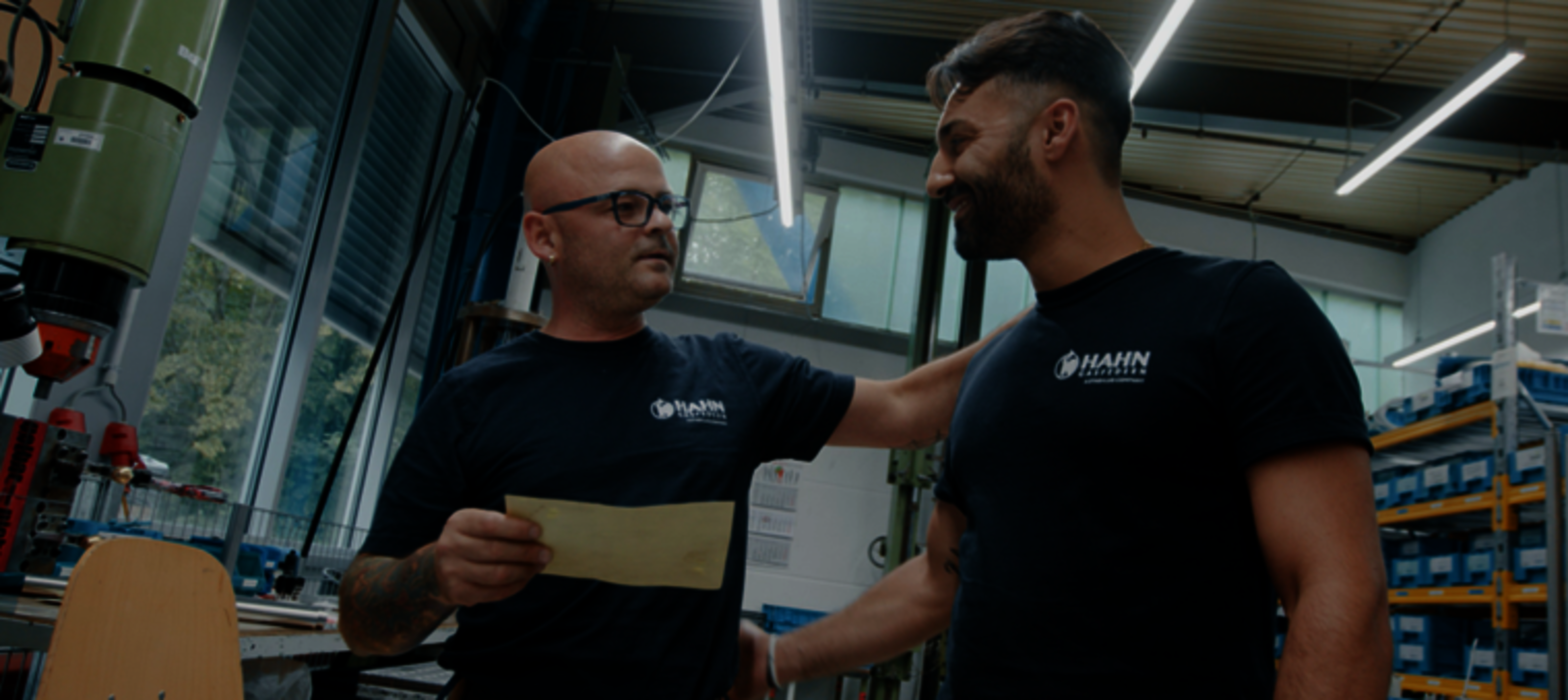 Zwei Mitarbeitende von Hahn Gasfedern in der Werkstatt, ein Mitarbeiter erklärt etwas und legt dem anderen unterstützend die Hand auf die Schulter.