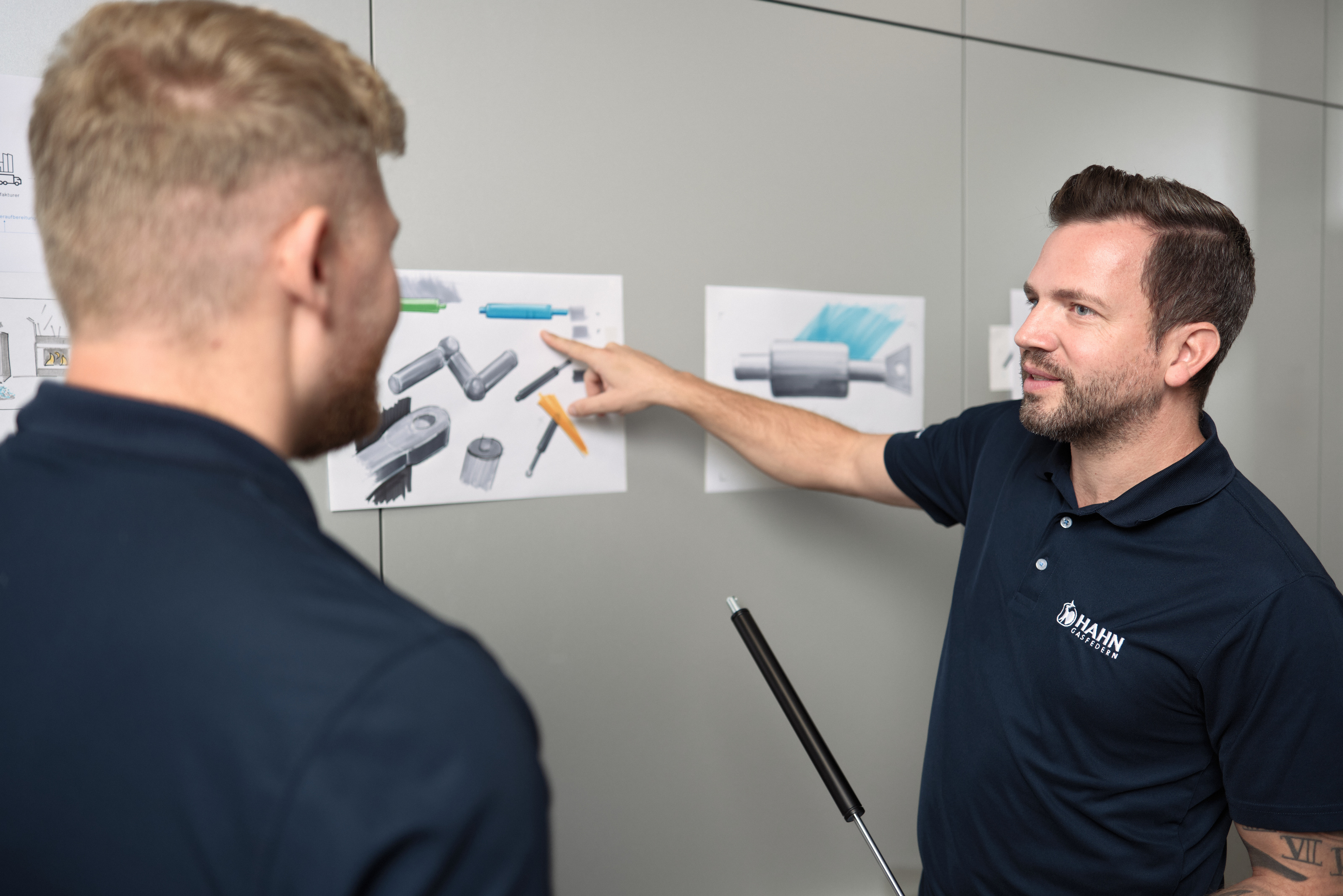 Zwei HAHN Gasfedern Mitarbeiter bei der Produktentwicklung, diskutieren innovative Lösungen mit technischen Zeichnungen.
